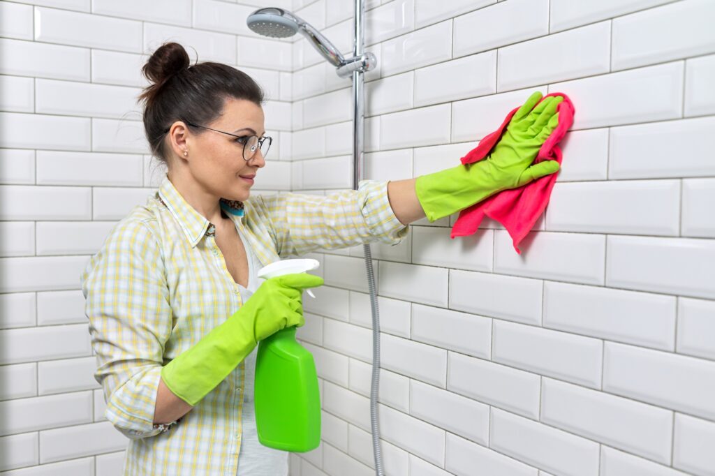 Bathroom cleaning, housewife washing white tile wall with detergent and rag