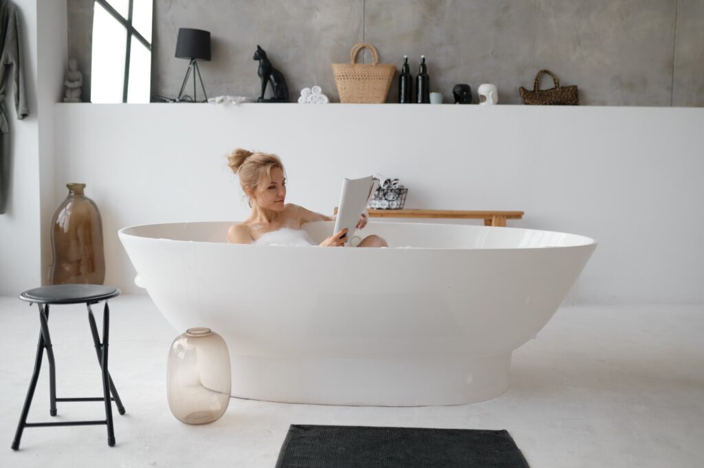 Beautiful young woman reading book or fashion magazine in bathtub
