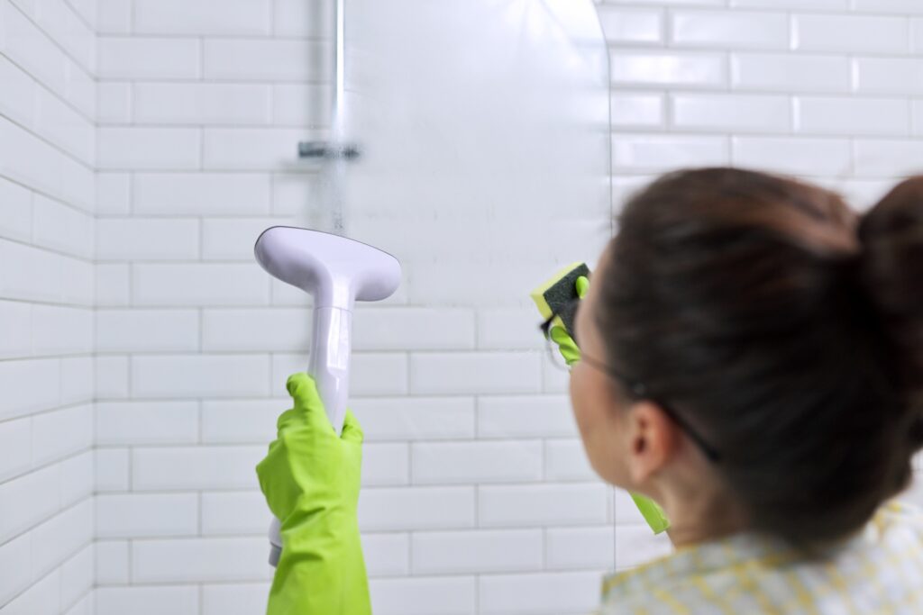 Woman cleaning in bathroom, washing glass with shower steam