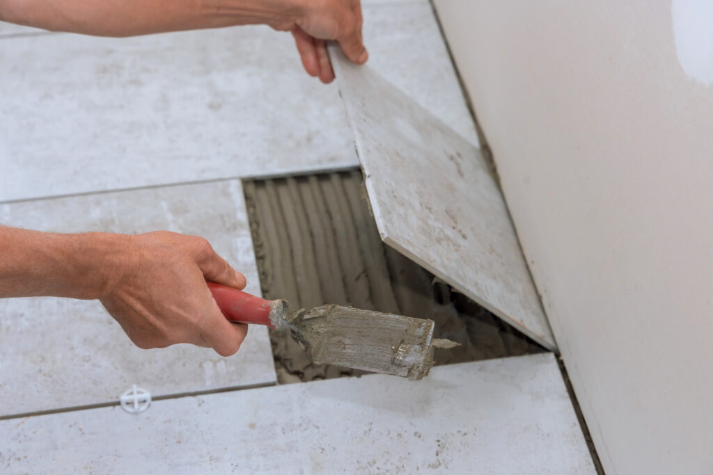 Bathroom tile repair in Panama City Beach — technician lifting a damaged floor tile and applying fresh thinset mortar.
