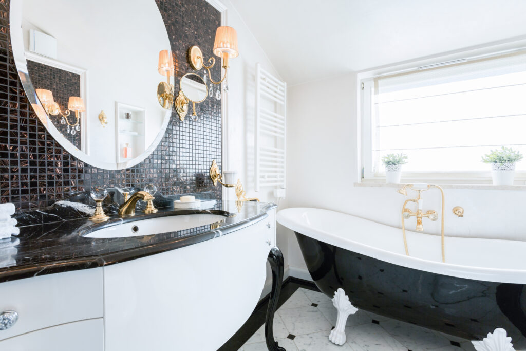 Elegant bathroom in Panama City Beach after repairs — black-and-white vanity, mosaic tile wall, and clawfoot tub with gold fixtures.
